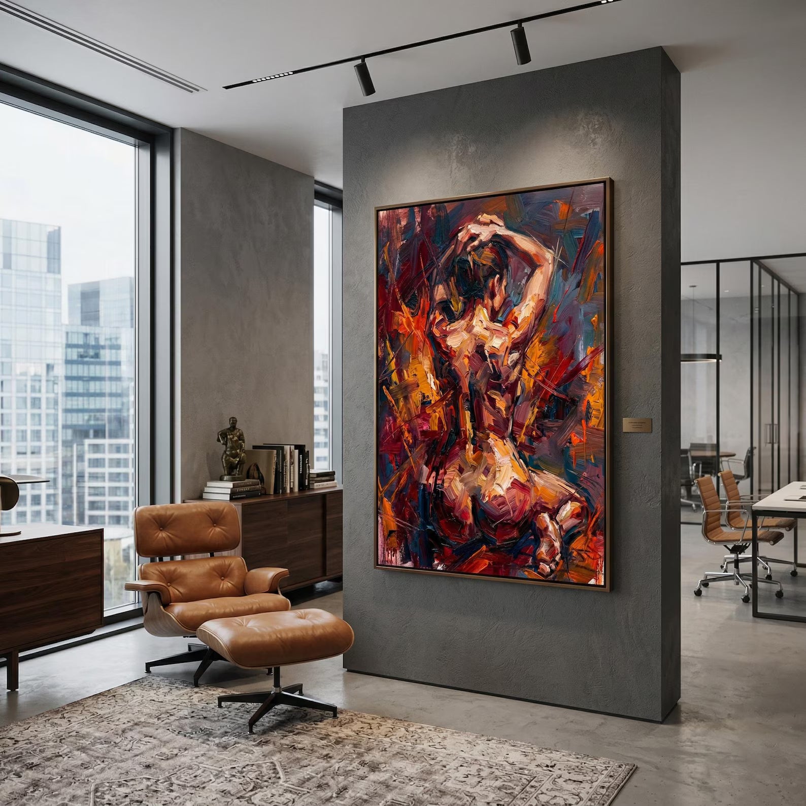 May include: An abstract oil painting of a figure with a warm color palette of reds, oranges, and yellows. The artwork is framed and hangs on a gray wall in a modern office setting. A brown leather chair and ottoman sit in front of the painting.