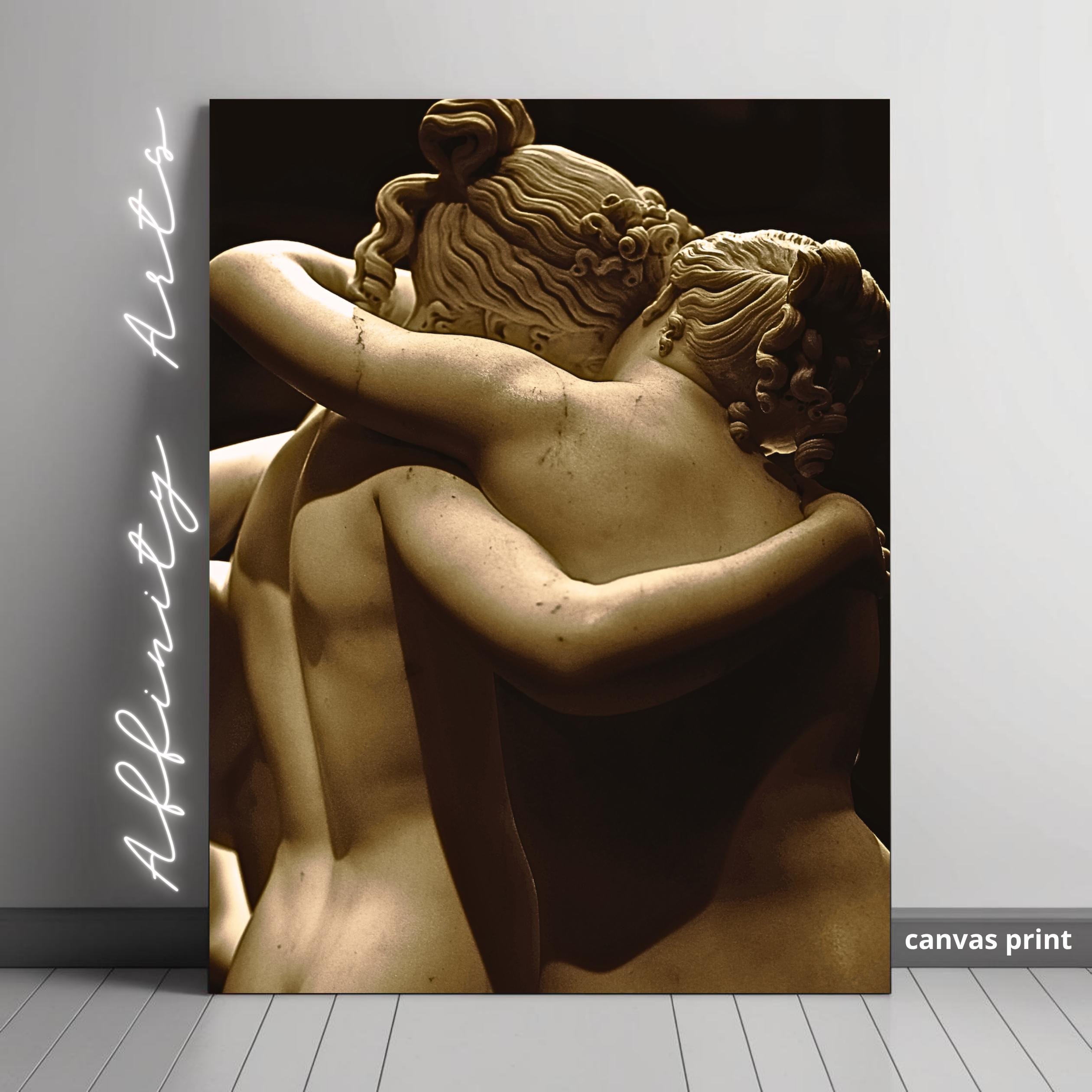 Antique statue detail: two women in embrace, backs visible, intricate hairstyles.